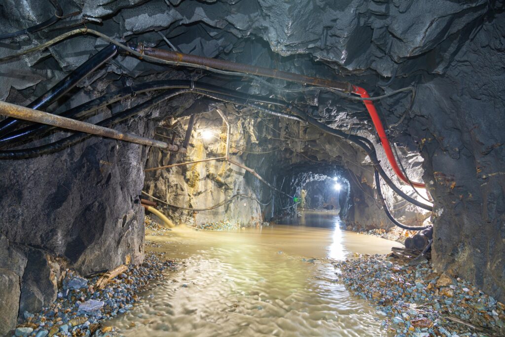 pexels photo 12032155 12032155 Dimly lit underground cave with flowing water and exposed pipes, showcasing rugged geology.